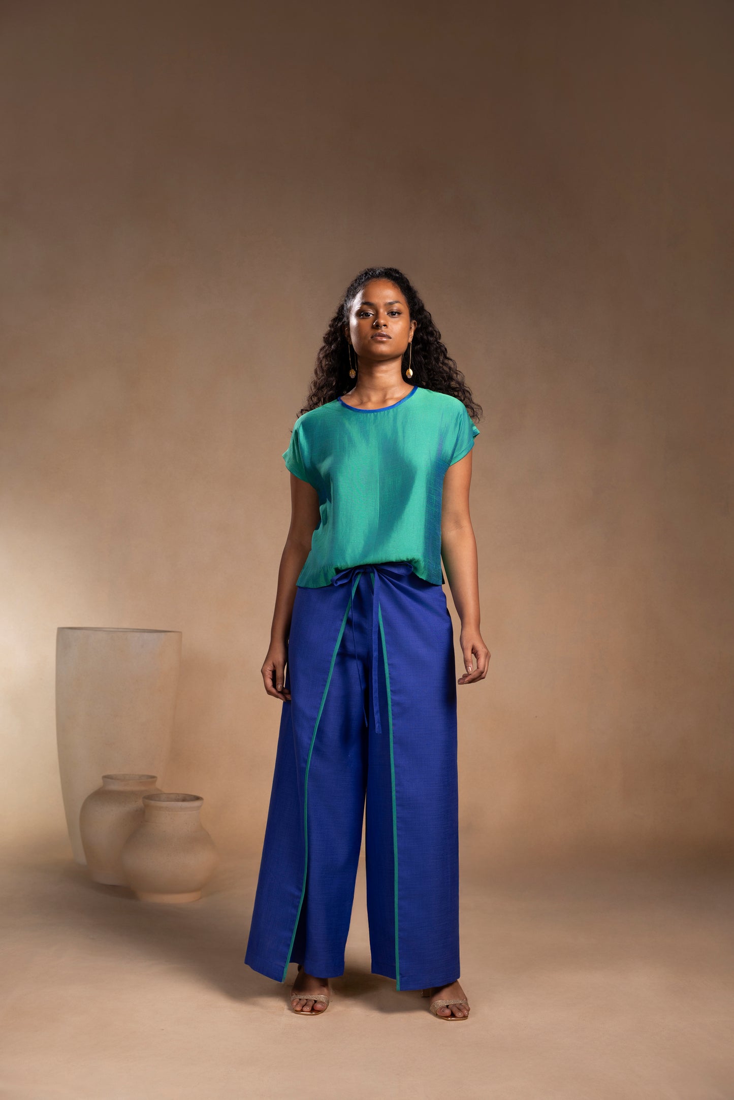 Woman wearing a green top and blue pants standing against a beige background