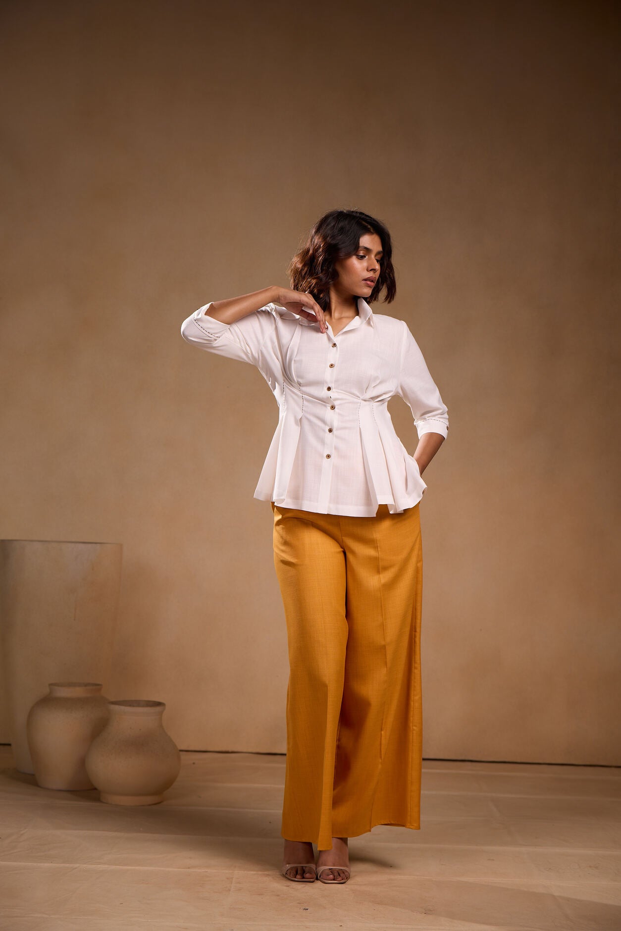 Woman wearing a white blouse and mustard pants against a beige background