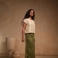 Woman wearing a beige top and green skirt standing against a beige wall with decorative vases.
