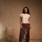 Woman wearing a beige top and brown skirt with floral embroidery against a beige background