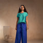 Woman wearing a green top and blue pants standing against a beige background
