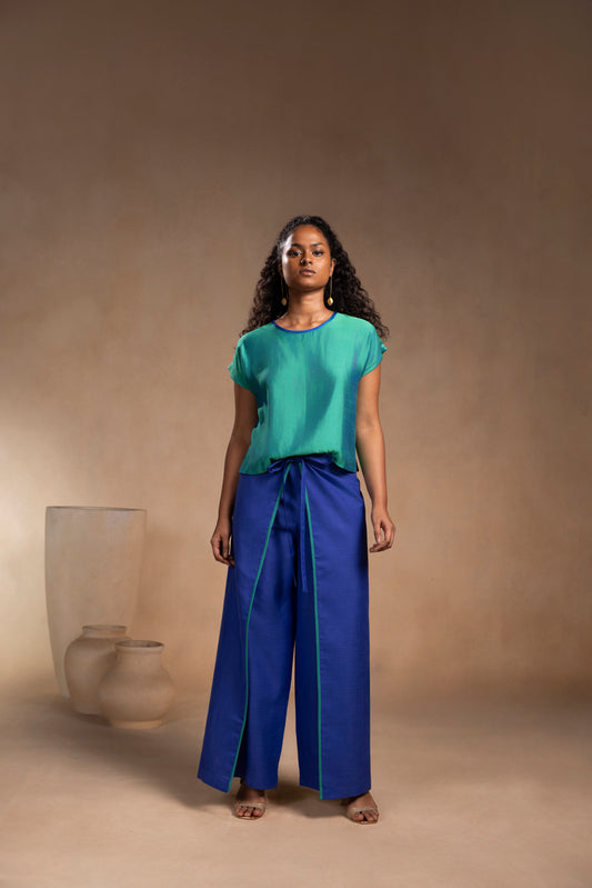 Woman wearing a green top and blue pants standing against a beige background
