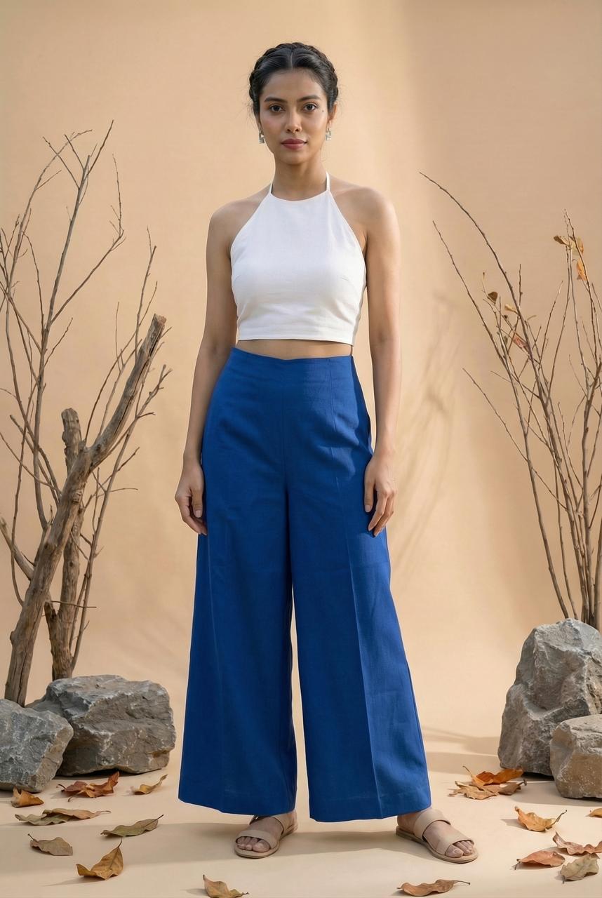Woman wearing a white top and blue pants standing in a natural setting with rocks and dry leaves.